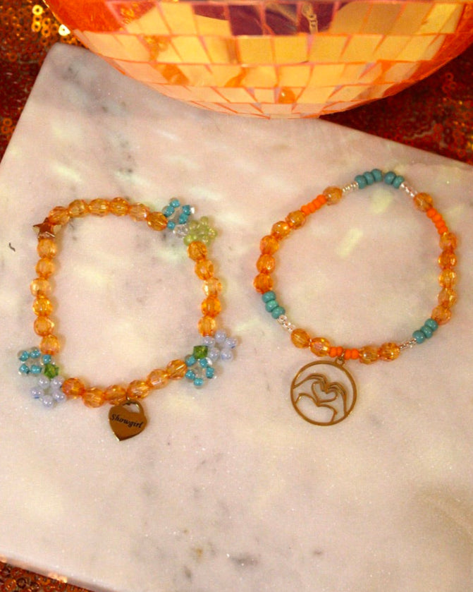 Two beaded bracelets on a marble surface with a decorative background.
